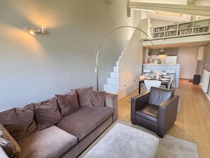 Ein modernes Wohnzimmer mit einer Couch, einem Sessel, einer Treppe und einer Küchenzeile.