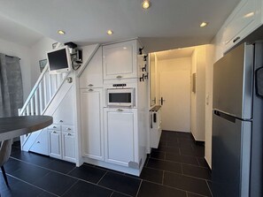 Eine Küche mit weißen Schränken, einem eingebauten Backofen, einem Kühlschrank und einer Treppe, die in eine andere Ebene führt.