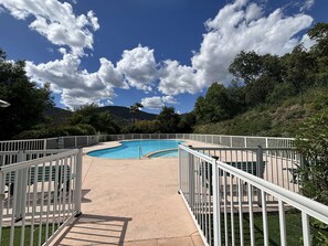 Ein Swimmingpool mit weißem Zaun, umgeben von viel Grün und einem klaren Himmel.