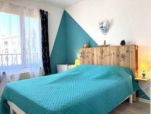 Ein Schlafzimmer mit einem Bett, einer Holzkommode, einem Fenster mit Vorhängen und einem an der Wand befestigten Kompass.
