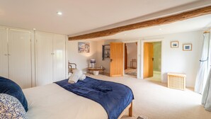 Un dormitorio con una cama, una puerta de madera, una silla, una mesita y un cuadro en la pared.