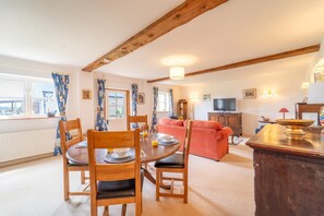 Ein gemütliches Wohnzimmer mit Essbereich, Holzmöbeln, einem Fernseher und Blick nach draußen.