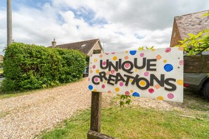 Ein Schild mit der Aufschrift 'UNIQUE CREATIONS', vor einem Haus mit Schotterweg und einem grünen Busch platziert.