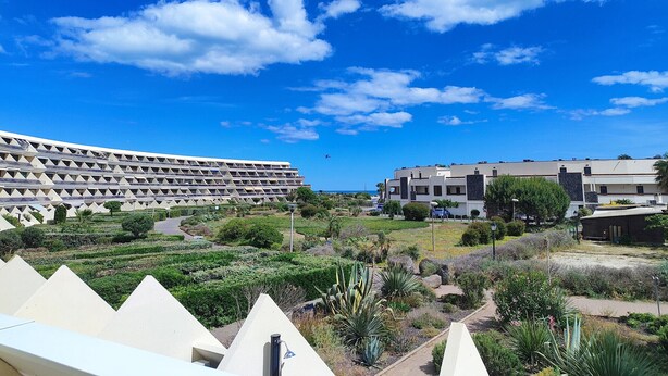 A modern building complex with multiple residential units, a landscaped garden area, and a clear blue sky with clouds. - Studio with AC and terrace - 2 guests (Cap d'Agde)