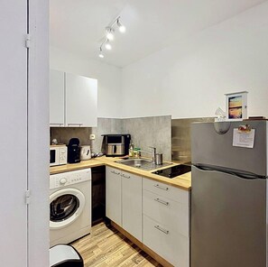 Eine kleine Küche mit Waschmaschine, Mikrowelle, Kaffeemaschine und Kühlschrank.
