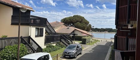 A residential street with two cars parked, a building with a red roof, and a body of water in the background.