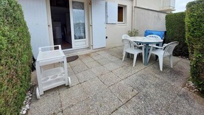 Eine Terrasse mit Tisch und Stühlen, ein überdachter Bereich mit einer Tür und ein kleiner Balkon.