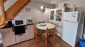 Eine kompakte Küche mit Esstisch, Holzstühlen, einer Mikrowelle, einer Kaffeemaschine, einem Schrank mit Glastüren und einem Kühlschrank.