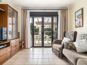 Ein Wohnzimmer mit Fernseher, Holzschrank, Sofa und einer Schiebetür zu einer Terrasse.