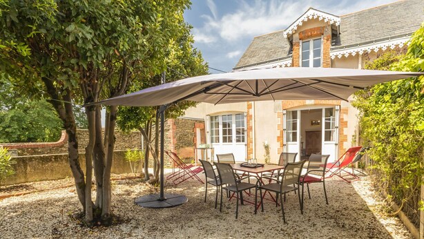 An outdoor patio with a table and chairs, a large umbrella, and a building with a stone wall and windows in the background. - Cozy cottage near the beach - 5 guests (Pornic)