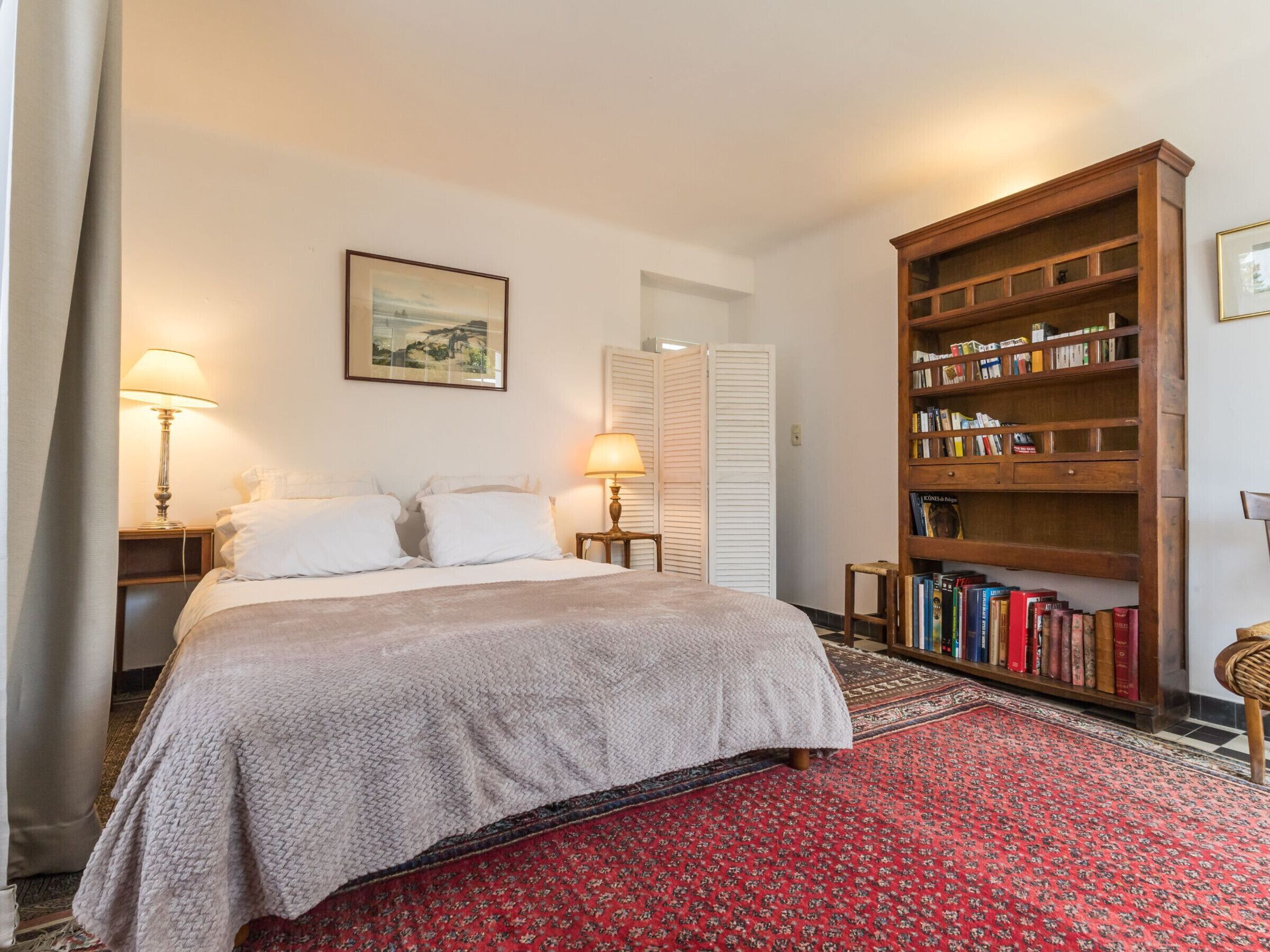 Ein Schlafzimmer mit einem Bett, zwei Nachttischlampen, einem Bücherregal und einem gerahmten Bild an der Wand.