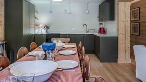 Ett modernt kök med mörka skåp, ett matbord för sex personer och en röd- och vitrutig duk.