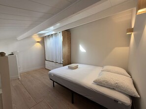 Ein Schlafzimmer mit einem Bett, einem Nachttisch, einem Holzschrank, einem Fenster mit Vorhängen und einem Oberlicht.