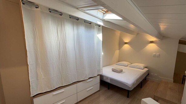 A bedroom with a bed, bedside tables, a wardrobe, a skylight, and a wall-mounted light fixture. - Duplex apartment, air conditioning, central - 4 guests (Port Leucate)
