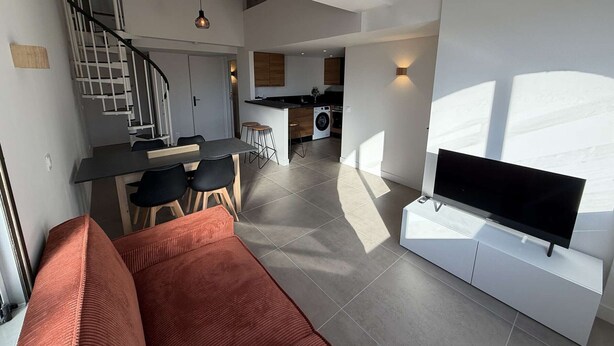 Una sala de estar moderna con un sofá, un televisor de pantalla plana y una escalera que lleva a una zona de cocina.