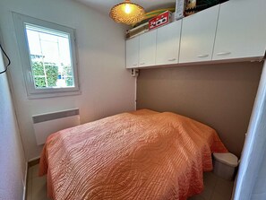 Ein kleines Schlafzimmer mit einem Einzelbett, einem Fenster, einer Heizung und einem weißen Kleiderschrank.