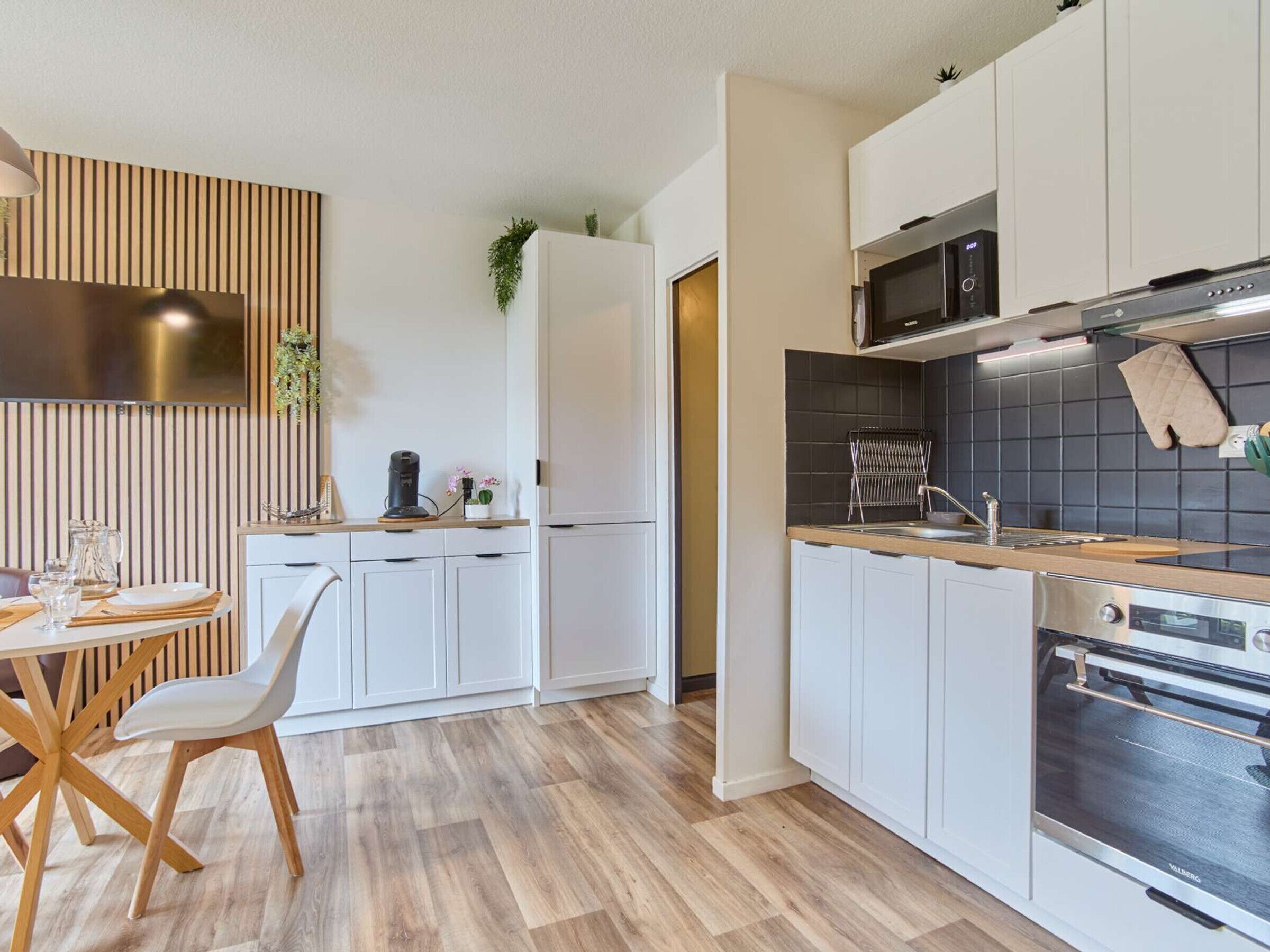 A modern kitchen with white cabinets, a wooden dining table, and a built-in oven.