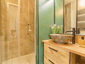 A bathroom with a glass shower enclosure, a wooden vanity with a stone basin, and a mirror reflecting a green wall. - Studio with balcony, parking, pets welcome - 2 guests (Barbotan-les-Thermes)