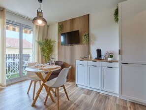 A modern kitchen with a dining area, a TV mounted on the wall, and a sliding glass door leading to an outdoor patio. - Studio with balcony, parking, pets welcome - 2 guests (Barbotan-les-Thermes)