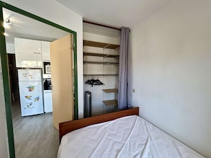 Ein Schlafzimmer mit Bett, Kleiderschrank, Spiegel und einer Tür zum Küchenbereich.