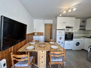 Eine kleine Küche mit Esstisch, Stühlen, Fernseher und grundlegender Ausstattung.