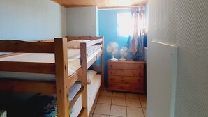 A small, single-bedded room with a wooden bunk bed, a small wooden dresser, and a window with curtains.