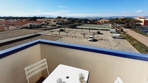 A balcony with a table and chair, overlooking a parking area and residential buildings.