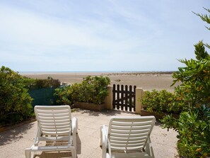 Zwei weiße Liegestühle mit Blick auf einen Strand und einen klaren Himmel.