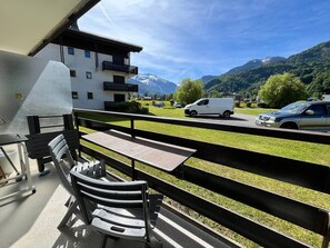 Ein Balkon mit Blick auf einen Berg, ein weißes Gebäude und abgestellte Autos.
