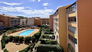 Un hotel con piscina rodeada de jardines cuidados, múltiples balcones y un cielo azul despejado.