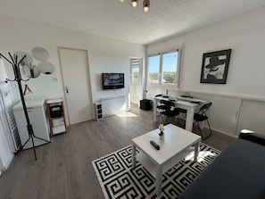 Una sala de estar moderna con un sofá blanco, una mesa de comedor y un televisor montado en la pared.