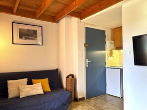 A room with a dark blue sofa, a framed picture on the wall, a door leading to a kitchen, and a television mounted on the wall. - Loft studio, AC, beach - 2 guests (La Londe-les-Maures)