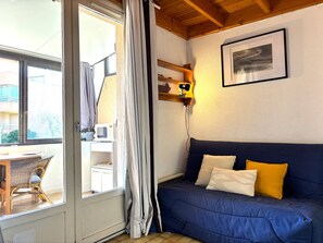 A room with a blue sofa, a white cabinet, a microwave, a framed picture on the wall, and a window with curtains. - Loft studio, AC, beach - 2 guests (La Londe-les-Maures)