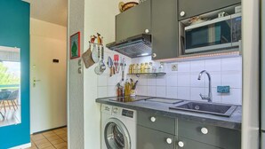 Een kleine keuken met een wasmachine, een magnetron en een spoelbak.