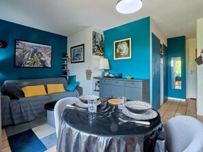 Ein modernes Wohnzimmer mit Esstisch für zwei Personen, einem grauen Sofa mit gelben Kissen und einem Stadtbild an der Wand.