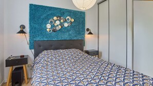 Een slaapkamer met een gebobbelde hoofdbord, een bed met een decoratief sprei, een wanddecoratie en twee bedlampen.