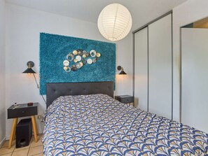 Ein Schlafzimmer mit einer gepolsterten Kopfteil, einer gemusterten Bettdecke, einem dekorativen Wandbild und zwei Nachttischlampen.