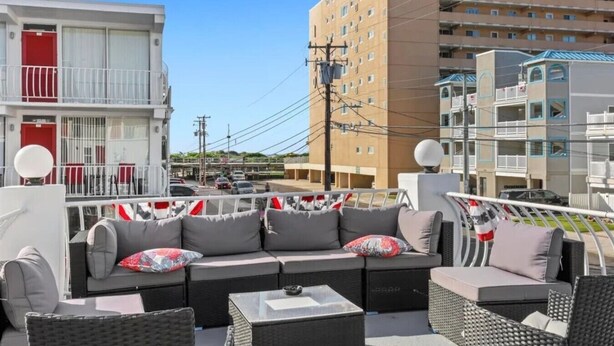 A rooftop terrace with outdoor furniture, a view of the cityscape, and a building with multiple floors. - Beach Block North Wildwood | Malibu Sun @ The Malibu (North Wildwood)