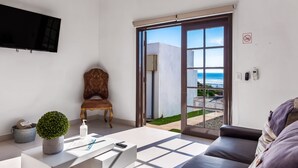 Un soggiorno moderno con un divano, un tavolino, una televisione e vista sul mare attraverso una porta scorrevole in vetro.