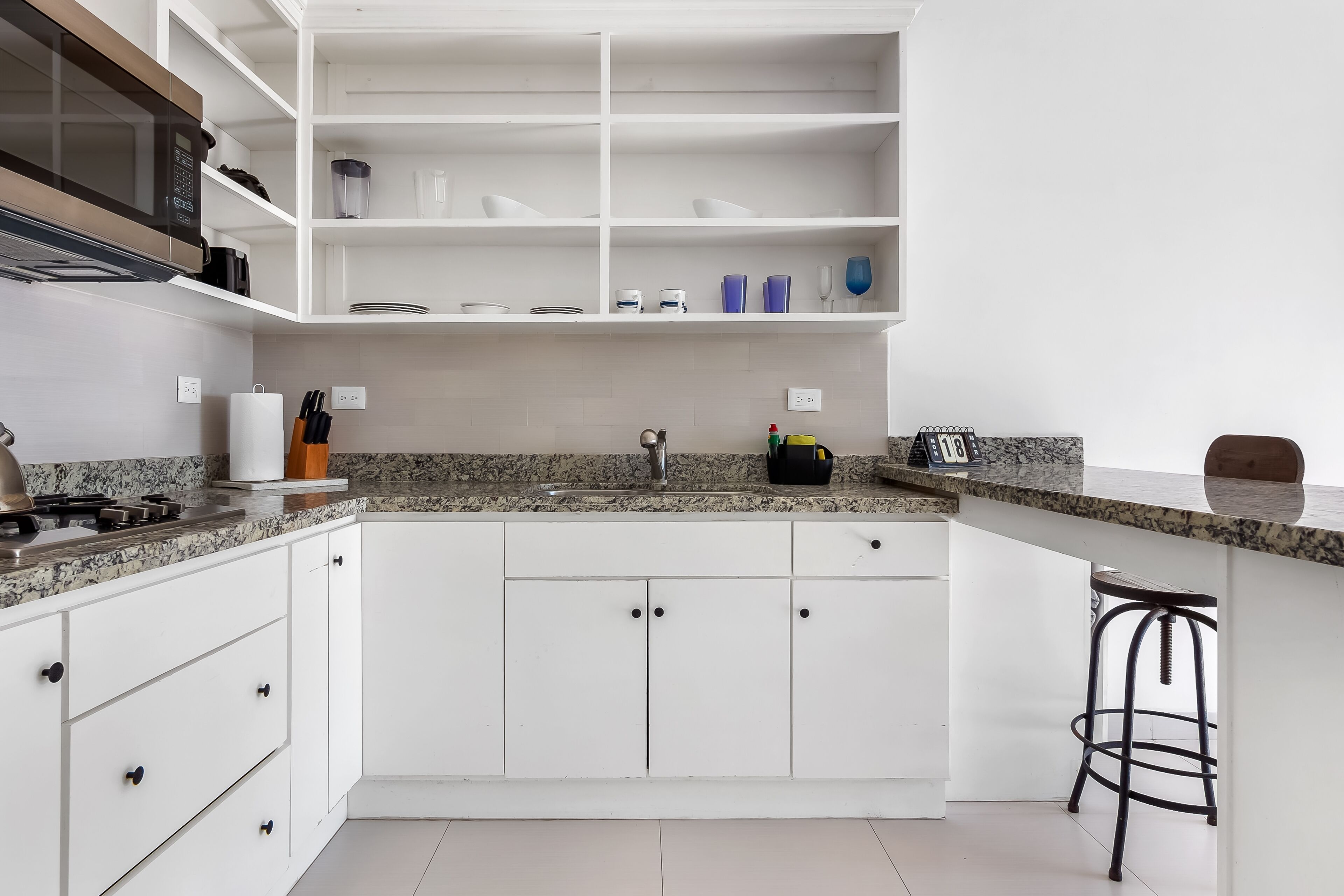 A modern kitchen with white cabinets, a granite countertop, a microwave, and a sink.
