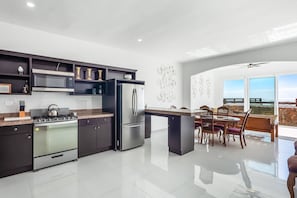 A modern kitchen with stainless steel appliances, dark cabinetry, and a dining area with a view. - Bright Dog-friendly Home With Heated Pool, Hot Tub, Streaming, & Ocean Views (Playas de Rosarito)