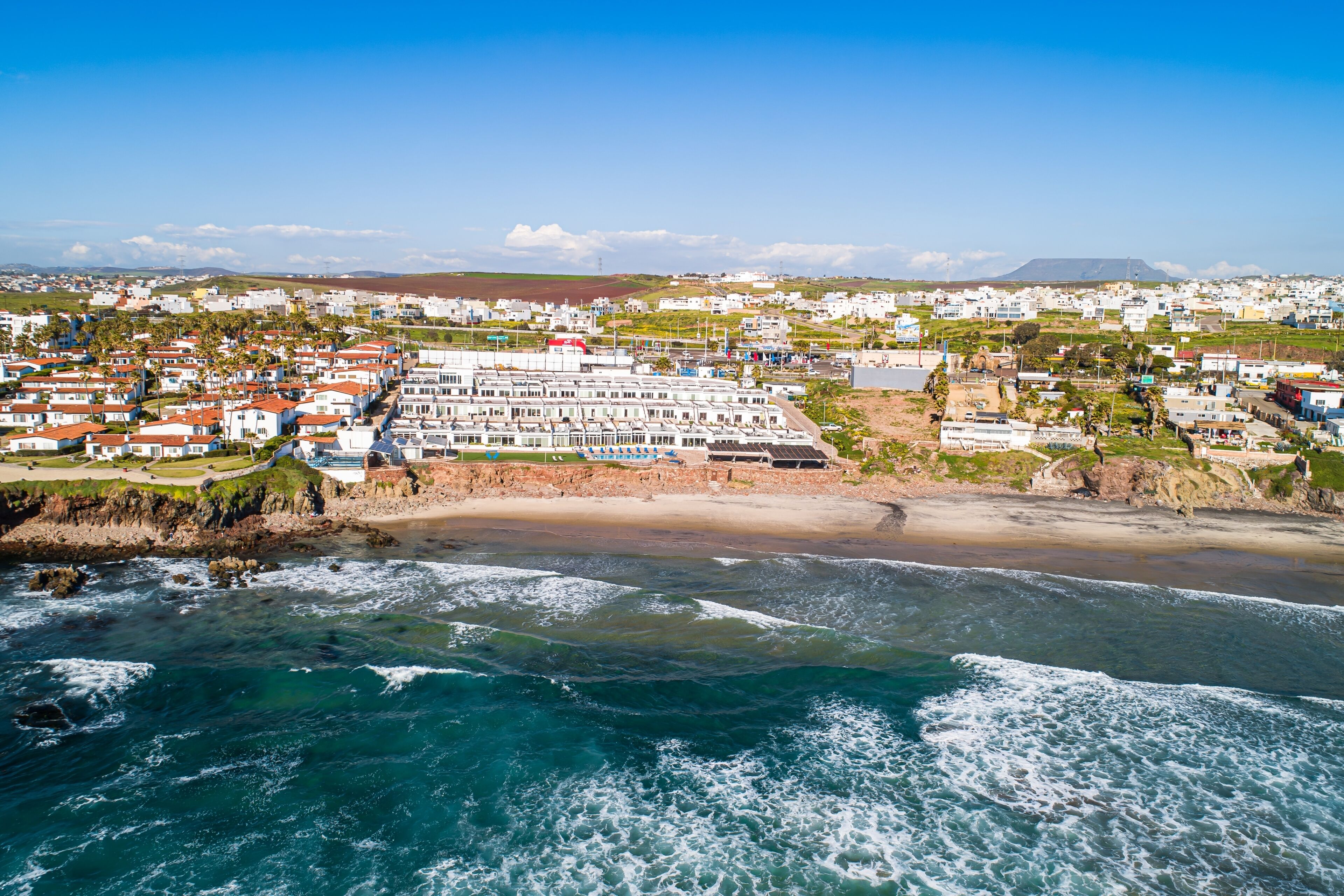 A coastal town with a beachfront hotel featuring multiple-story buildings, a sandy beach, and ocean waves.