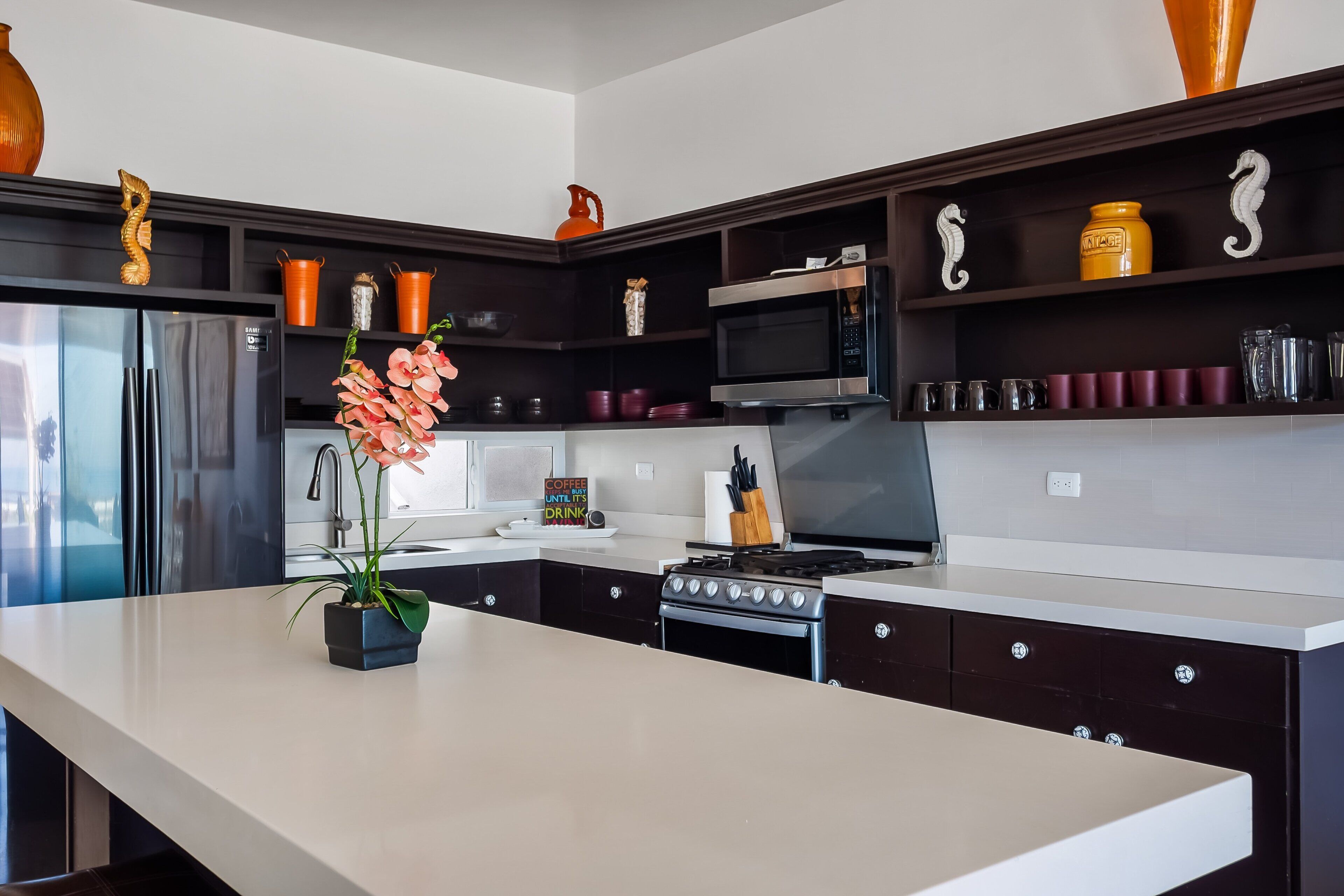 Una cocina moderna con una isla central, electrodomésticos de acero inoxidable y objetos decorativos en estantes.