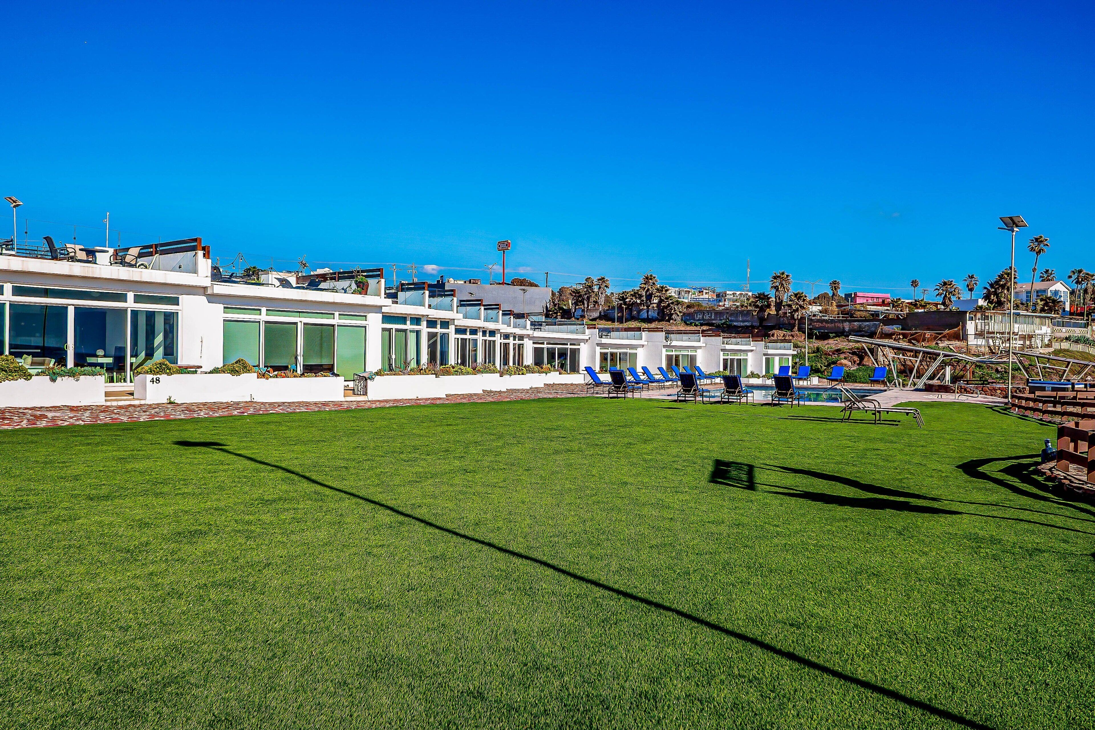 A modern building with a pool area, including a grassy lawn and blue chairs.