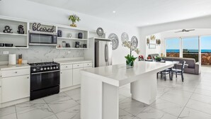 A modern kitchen with white cabinetry, a central island, and a dining area with a view. - Dog-friendly Home With Heated Outdoor Pool, Hot Tub, Balcony, Rooftop Terrace (Playas de Rosarito)