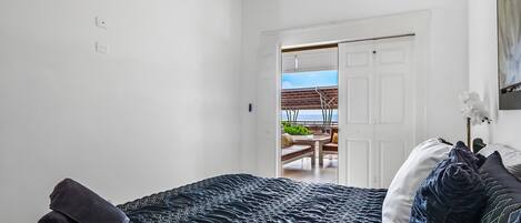 A bedroom with a bed, a door leading to a balcony, and a view of the outdoors.