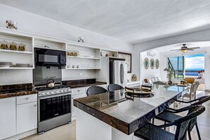 Eine moderne Küche mit weißen Schränken, einer zentralen Kochinsel und Meerblick.