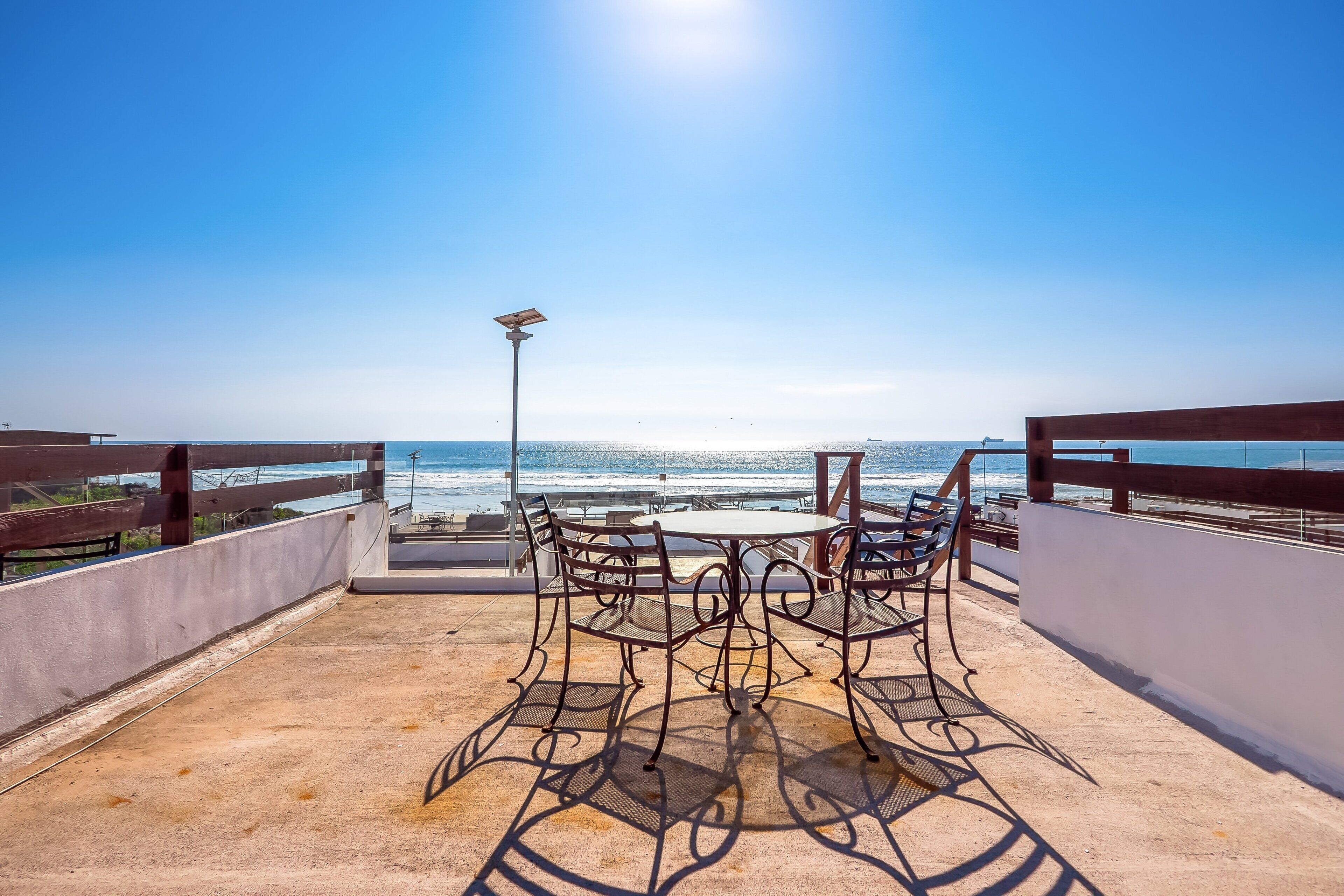 A rooftop terrace with a table and chairs, a railing, and a view of the ocean.