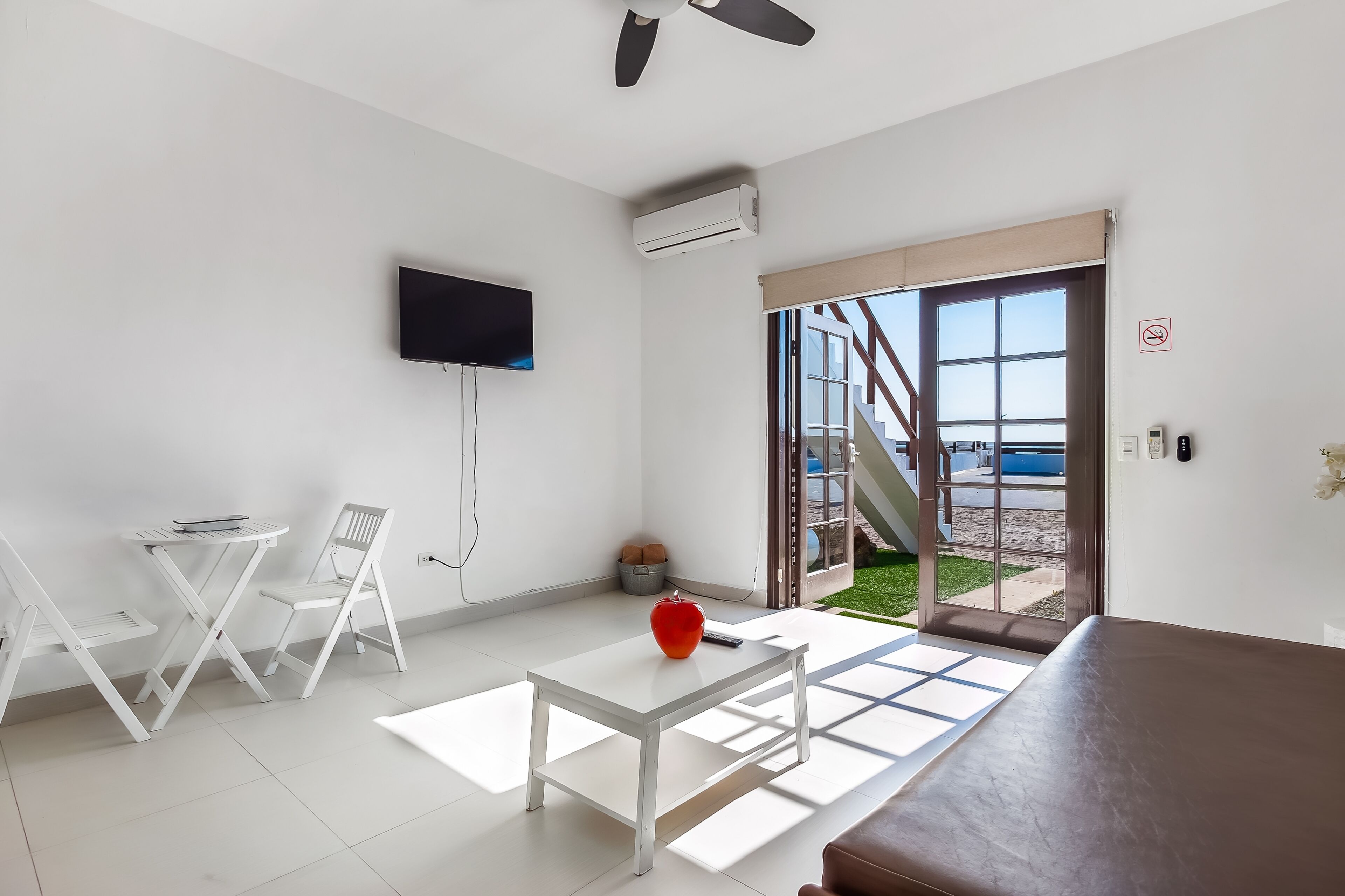 Una sala de estar moderna con un televisor de pantalla plana, una mesa blanca y una manzana roja sobre la mesa.