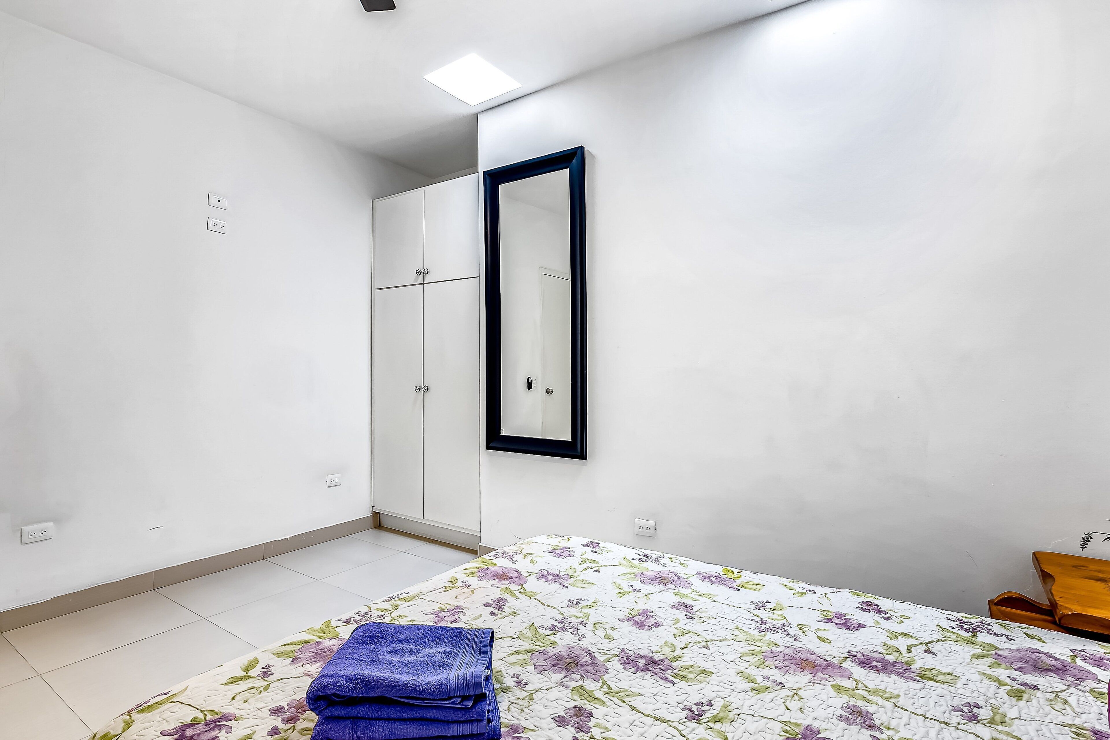 A bedroom with a bed, a wardrobe, a mirror, and a small wooden table.